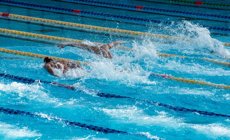Frontal view of a competitive swimmer mid-breaststroke in a clear blue pool, water droplets suspended mid-air, sunlit surface